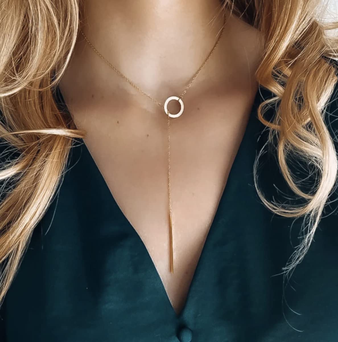 Frau mit goldener Y-Halskette, Kreisanhänger, elegantes Schmuckdesign, schwarzes Oberteil.