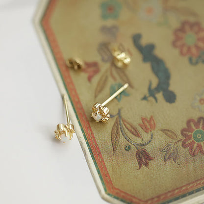 Goldene Ohrringe mit Perlen auf floralem Hintergrund, eleganter Schmuck, modische Accessoires.