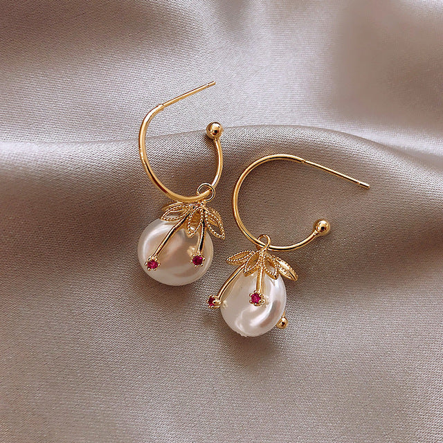 Goldene Ohrringe mit Perlen und roten Steinen, elegantes Design, Schmuck für Damen.