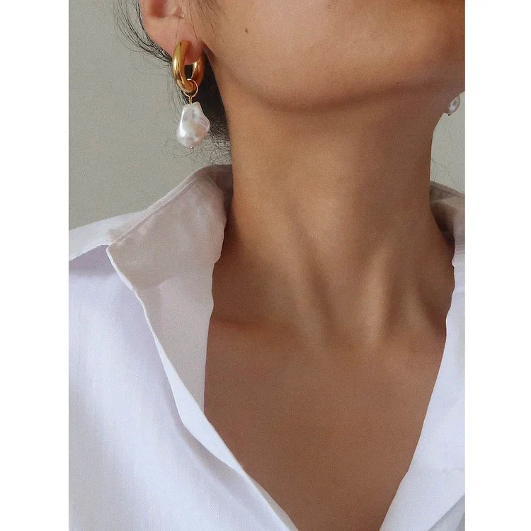 Frau mit goldenen Ohrringen und Perlenanhänger, weißes Hemd, eleganter Schmuck, Nahaufnahme.