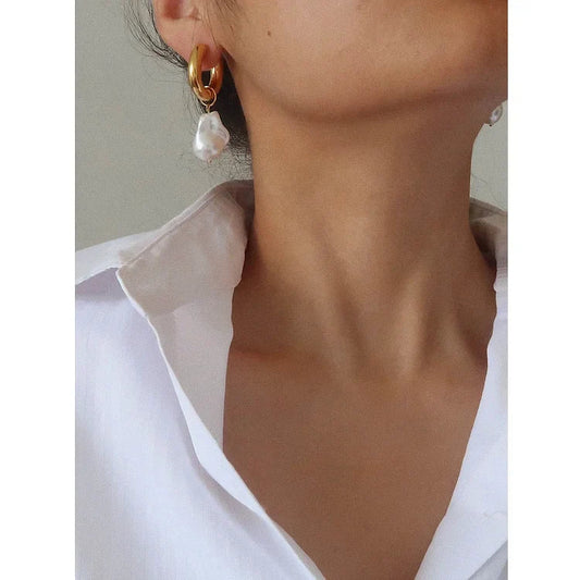 Frau mit goldenen Ohrringen und Perlenanhänger, weißes Hemd, eleganter Schmuck, Nahaufnahme.