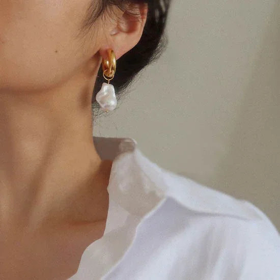 Goldene Creolen mit weißen Perlenanhängern, eleganter Schmuck für Damen, Nahaufnahme.