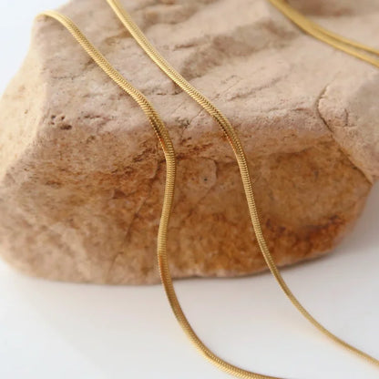 Goldene Schlangenkette auf Stein, elegantes Schmuckdesign, modisches Accessoire für Damen.