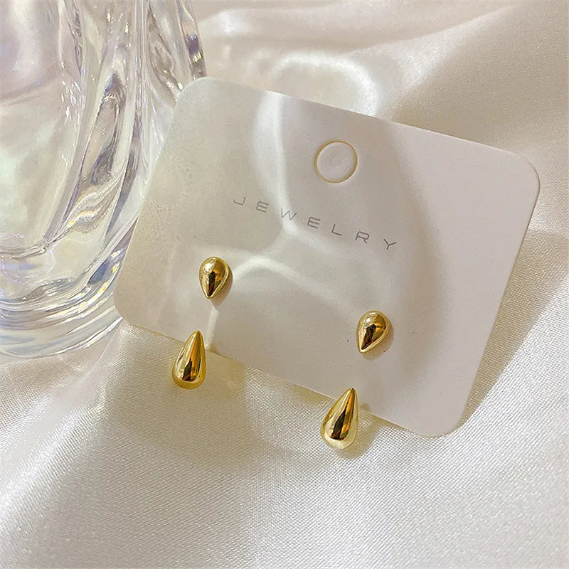 Goldene Tropfen-Ohrringe auf Schmuckkarte, glänzend, elegant, modisch, auf weißem Satin.
