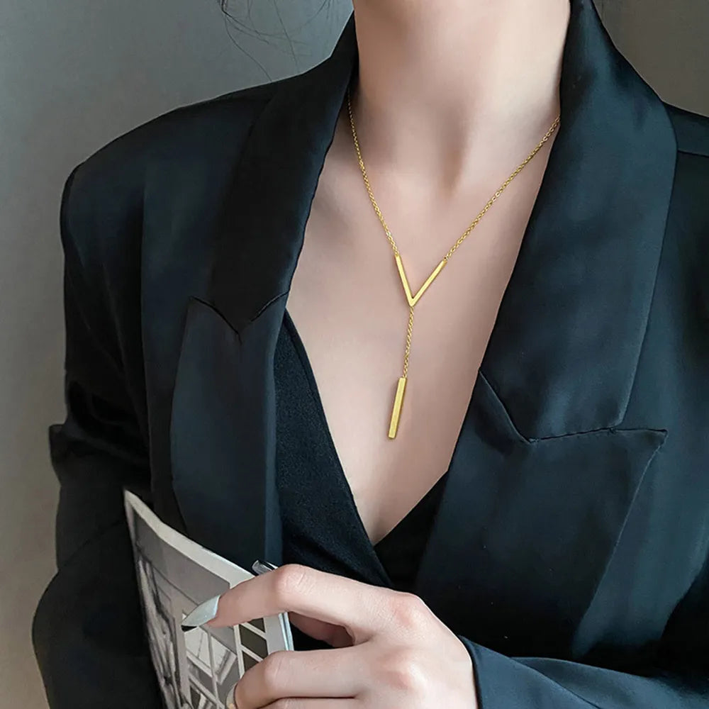 Frau mit schwarzem Blazer trägt goldene V-förmige Halskette, elegantes Schmuckdesign.