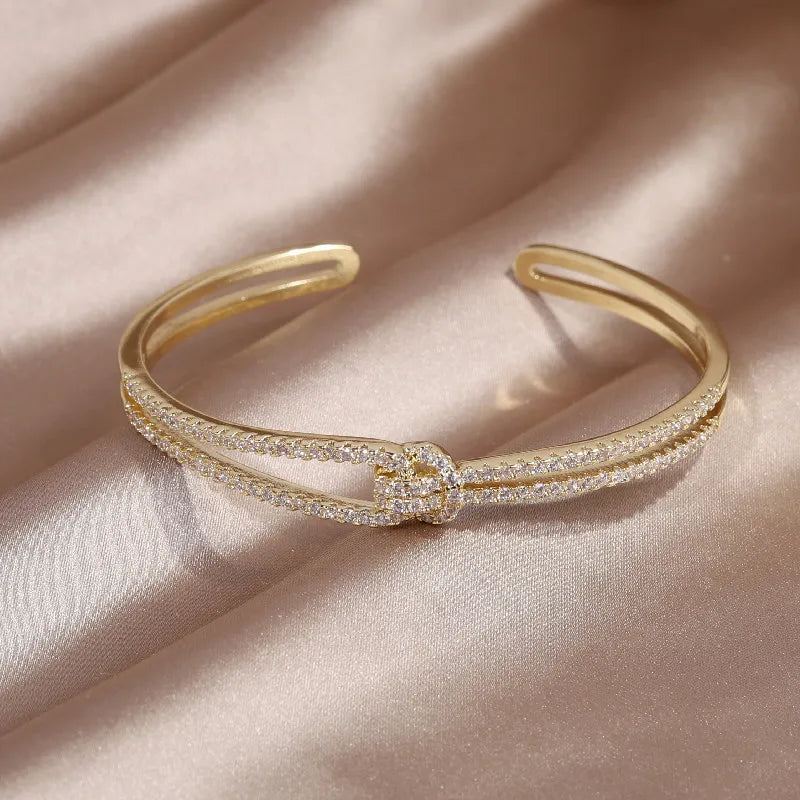 Goldenes Armreif mit Strasssteinen, elegantes Schmuckstück auf beigem Stoffhintergrund.