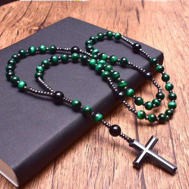 Schwarzer Rosenkranz mit grünen Perlen und Kreuz auf Holztisch, religiöses Schmuckstück.