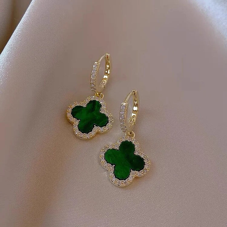Goldene Ohrringe mit grünem Kleeblatt-Anhänger auf Seide, eleganter Schmuck, Damenaccessoire.