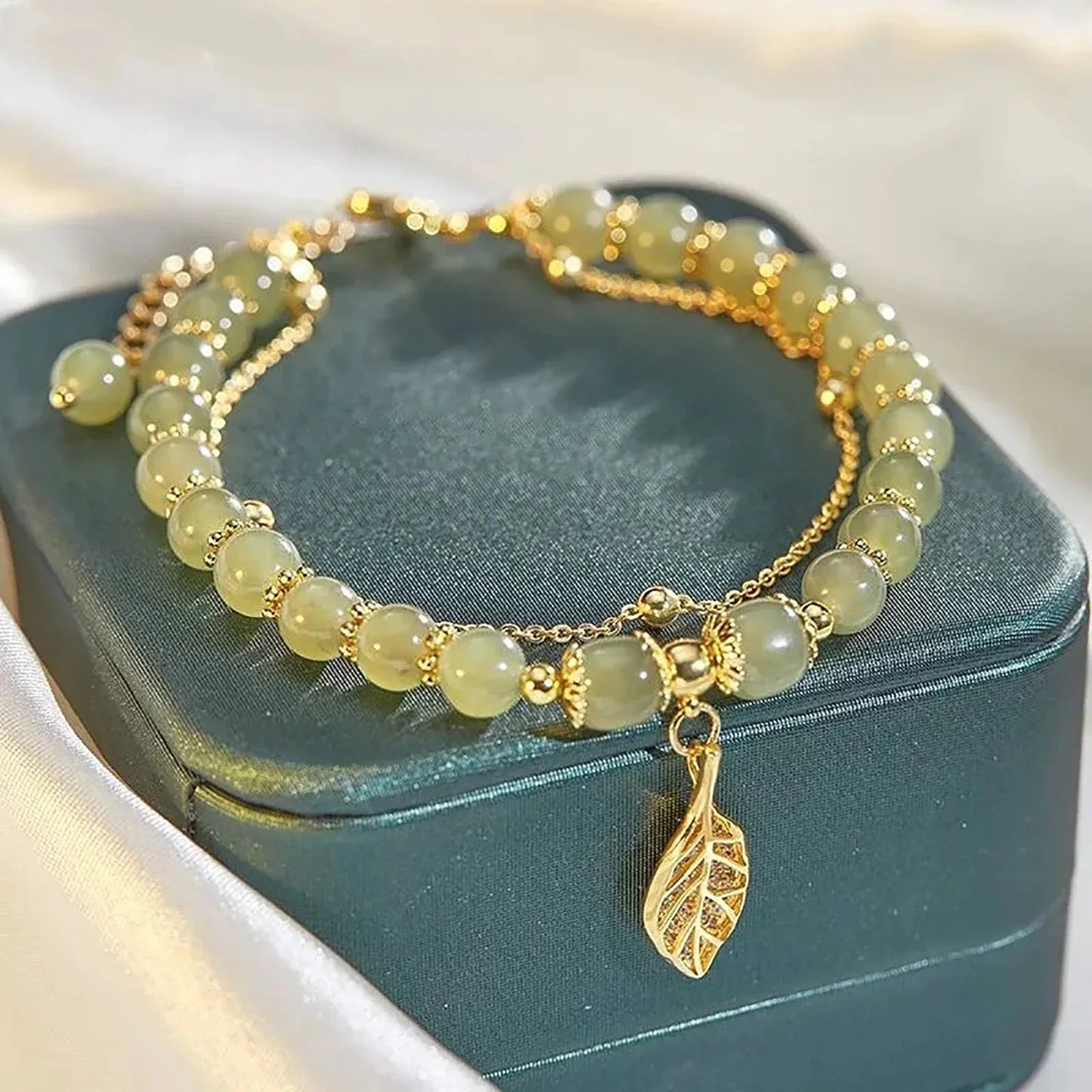 Grünes Perlenarmband mit goldfarbenem Blattanhänger auf Schmuckschatulle.