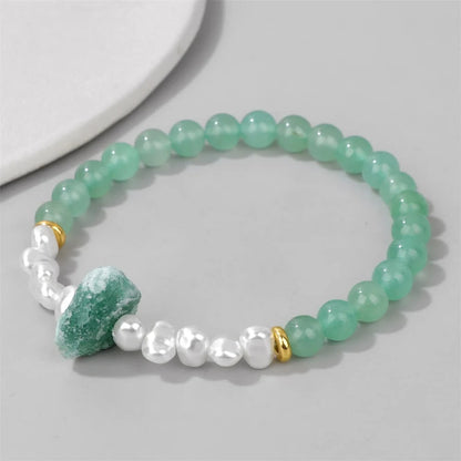 Grünes Aventurin-Perlenarmband mit weißen Perlen und goldenen Akzenten auf grauem Hintergrund.
