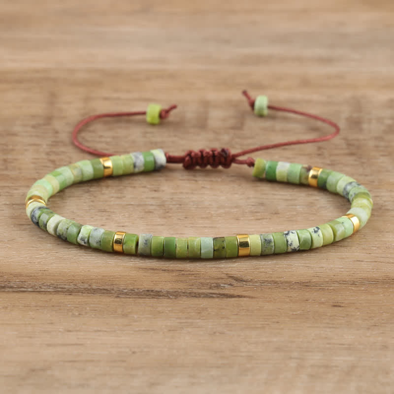 Grünes Perlenarmband mit goldenen Akzenten, verstellbar, handgefertigt, auf Holzoberfläche.
