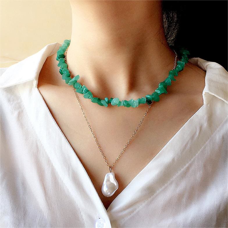 Grüne Edelstein-Halskette und goldene Perlenkette auf weißer Bluse, eleganter Schmuck.