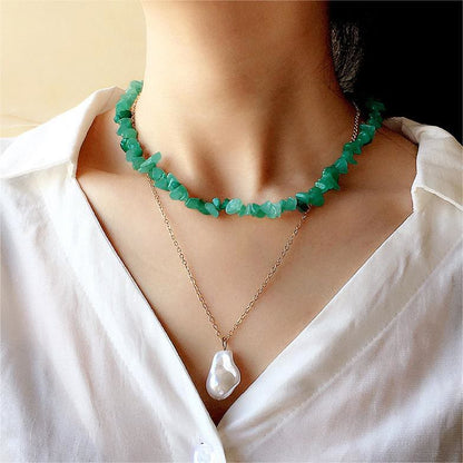 Grüne Edelstein-Halskette und goldene Perlenkette auf weißer Bluse, eleganter Schmuck.