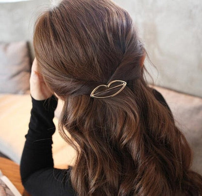Frau mit braunem Haar, goldene Haarspange in Lippenform, elegantes Accessoire, Rückansicht.