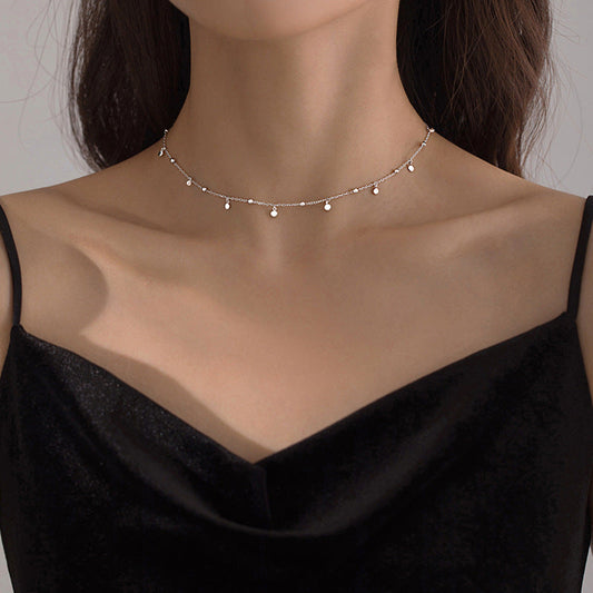 Frau mit schwarzem Kleid trägt elegantes, silbernes Perlenhalsband, minimalistisch, modisch.