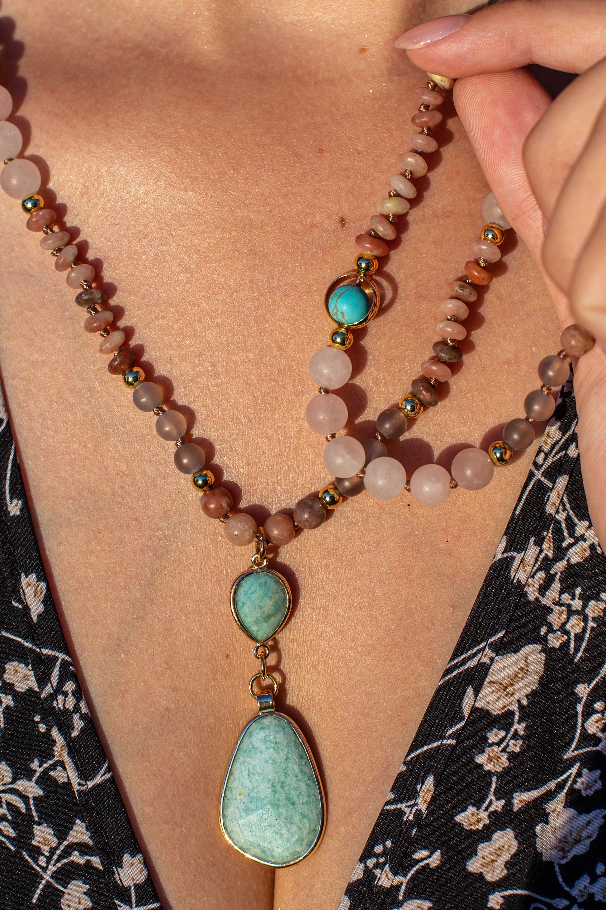 Frau mit Halskette aus Rosenquarz und türkisfarbenem Anhänger, eleganter Schmuck, Nahaufnahme.