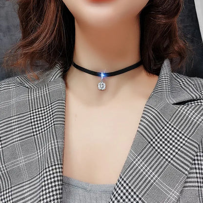 Frau mit schwarzem Choker-Halskette und funkelndem Anhänger, kariertes Sakko, modisch.