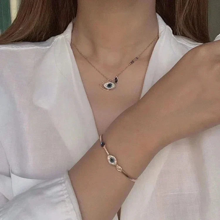 Frau mit weißer Bluse trägt elegantes Auge-Anhänger-Halskette und Armband, modischer Schmuck.