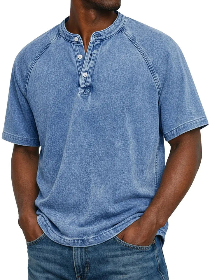 Mand i lyseblå vasket Henley-T-shirt med raglanærmer og tre knapper i halsen, kombineret med blå jeans. 2