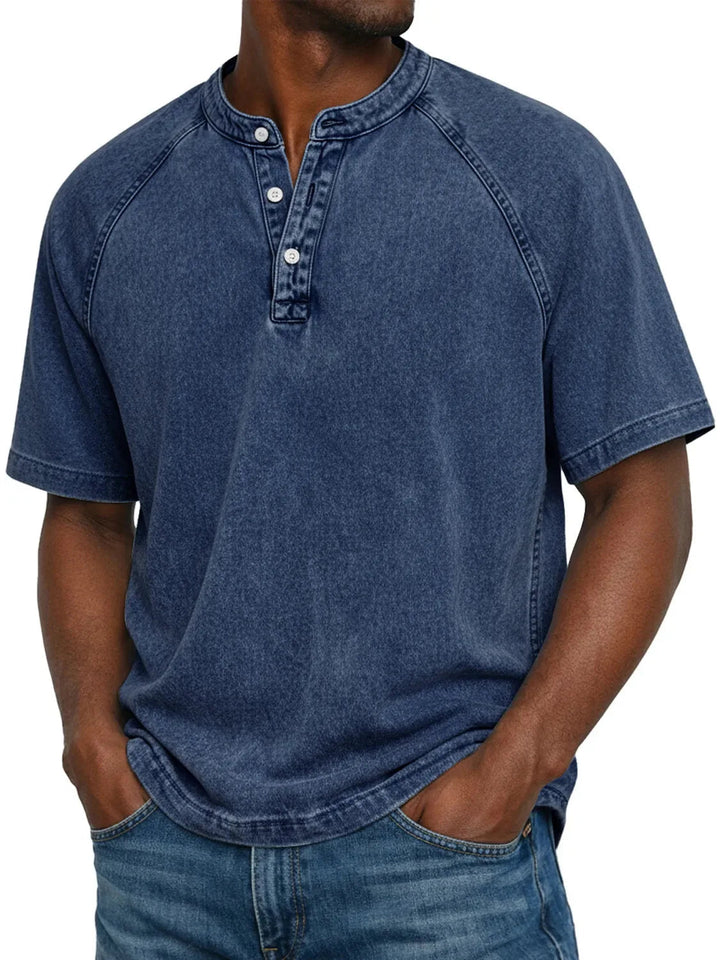 Mand i mørkeblå vasket Henley-T-shirt med raglanærmer, knaplukning og kontrastsyninger, hænderne i jeanslommerne. 3