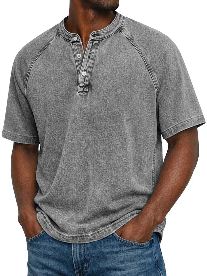 Mand i grå vasket Henley-T-shirt med raglanærmer og knaplukning ved halsen, båret med blå jeans. 4