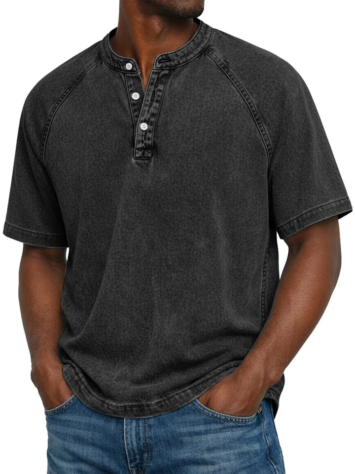 Mand i sort vasket Henley-T-shirt med raglanærmer og hvide knapper i halsen, båret med blå jeans. 5