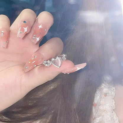 Frau mit langen, verzierten Acrylnägeln und silbernem Herzring, modisches Nageldesign.