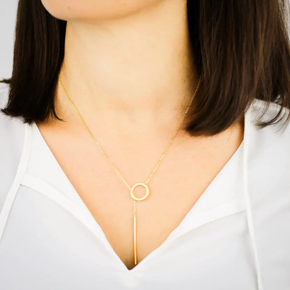 Frau mit goldener Halskette, Kreisanhänger, minimalistischer Schmuck, weißes Oberteil.