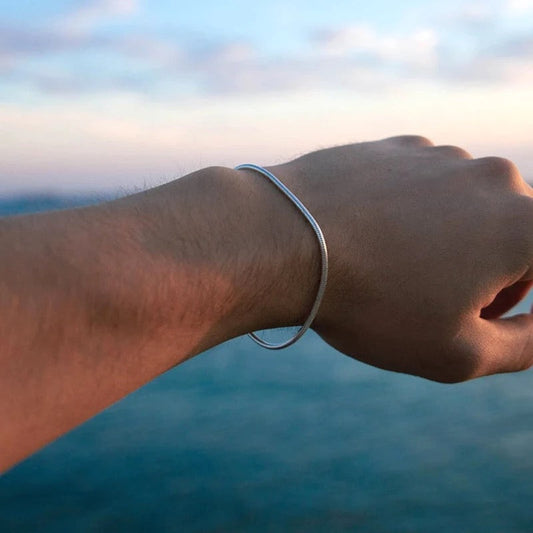 Silberarmband am Handgelenk vor Meereshorizont, minimalistisches Schmuckdesign.