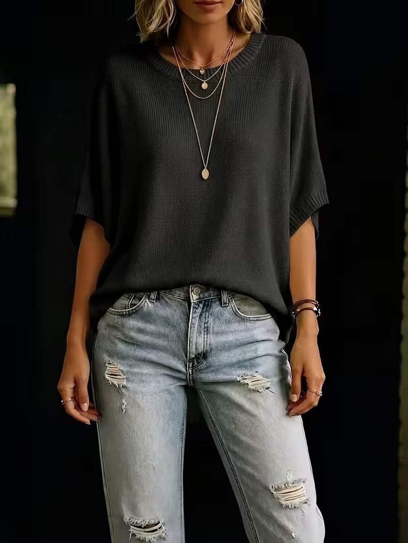 Sort strikbluse med løs pasform set forfra på model sammen med lyse jeans med flænger og lange halskæder. 27