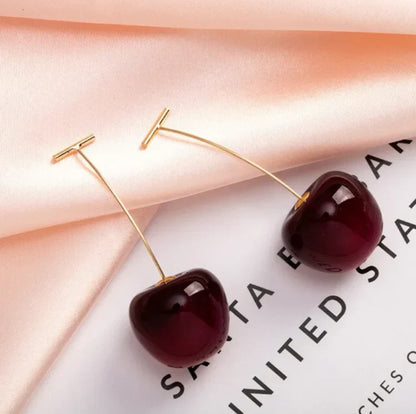 Kirschohrringe aus Gold und rotem Harz auf rosa Stoff, modisches Accessoire für Damen.