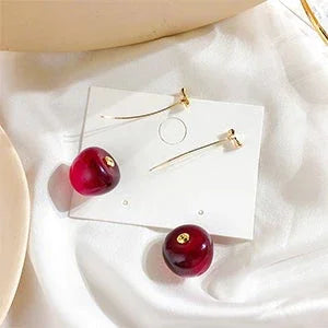 Goldene Ohrringe mit Kirsch-Design auf weißem Stoff, eleganter Schmuck, minimalistisch.