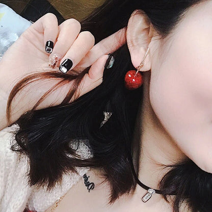 Frau mit roten Kirsch-Ohrringen, schwarze Nägel, modisches Accessoire, Nahaufnahme.
