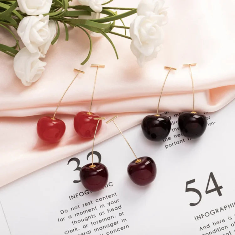Kirschohrringe auf rosa Stoff mit weißen Blumen, modische Accessoires, rot und dunkelrot.