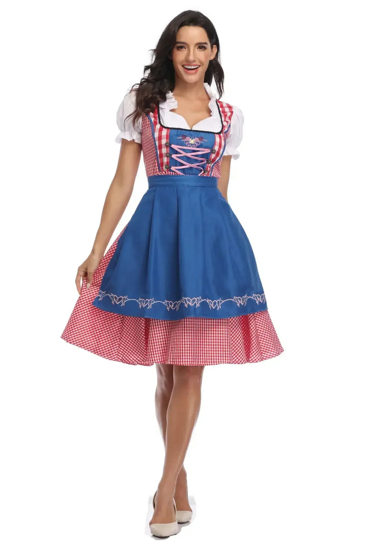 Model i rødternet dirndl med blåt broderet forklæde og lyserød snøring, set forfra med let svungen nederdel. 7