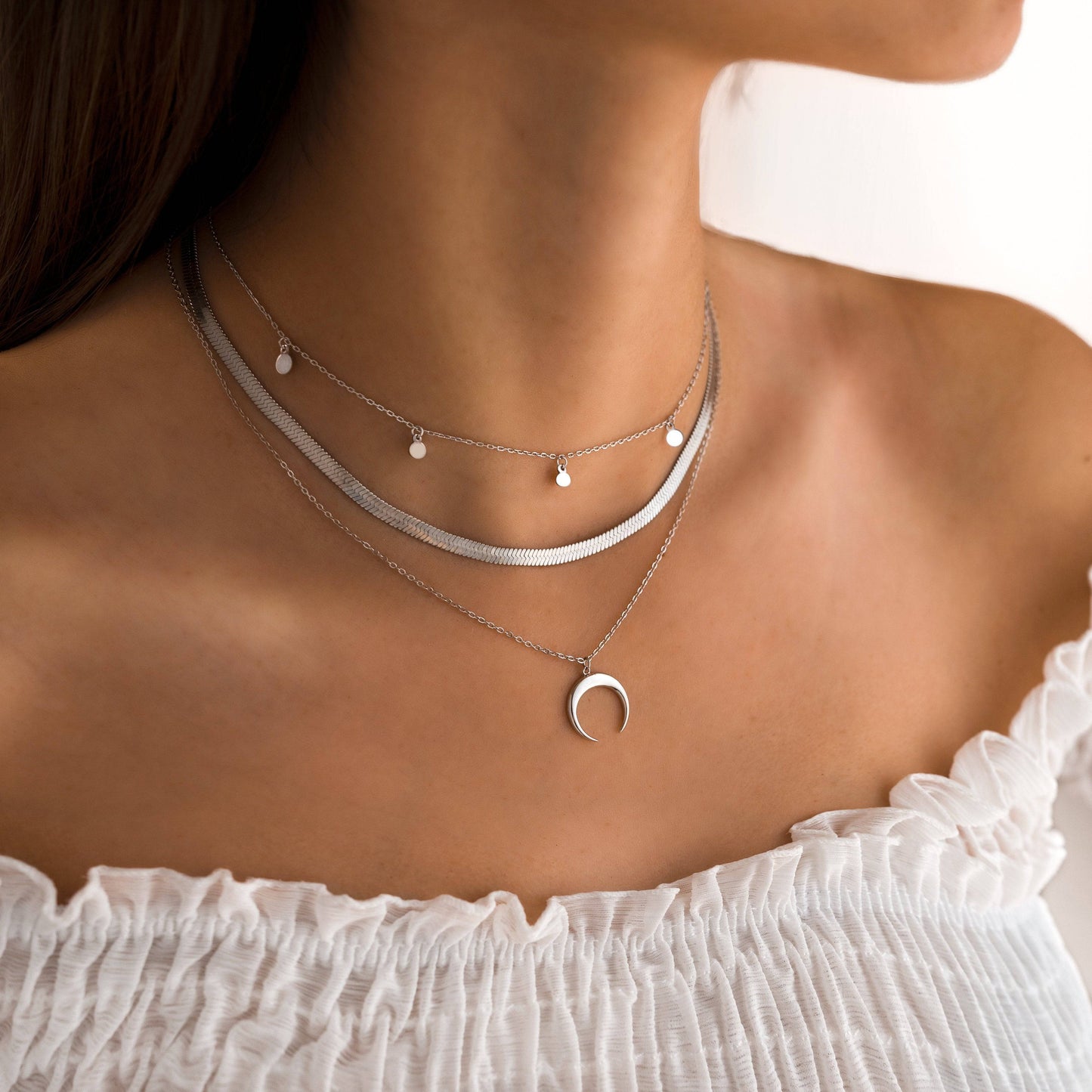 Frau trägt silberne Halsketten mit Mondanhänger, modischer Schmuck, elegantes Design.