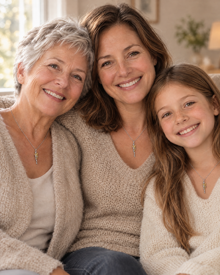 Tre generationer af kvinder, bedstemor, mor og barn, sidder tæt sammen og bærer hver en halskæde med samme vedhæng. 5