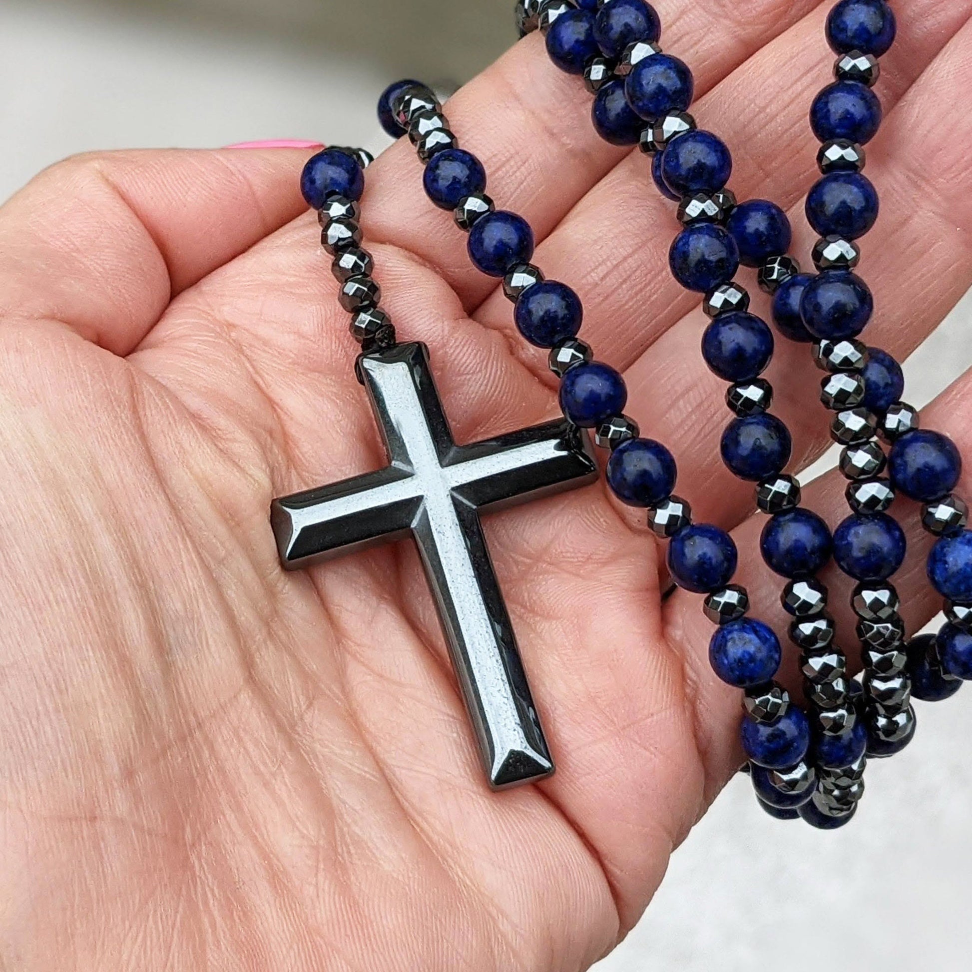 Hand hält blauen Rosenkranz mit schwarzem Kreuzanhänger, religiöses Schmuckstück, Gebetskette.