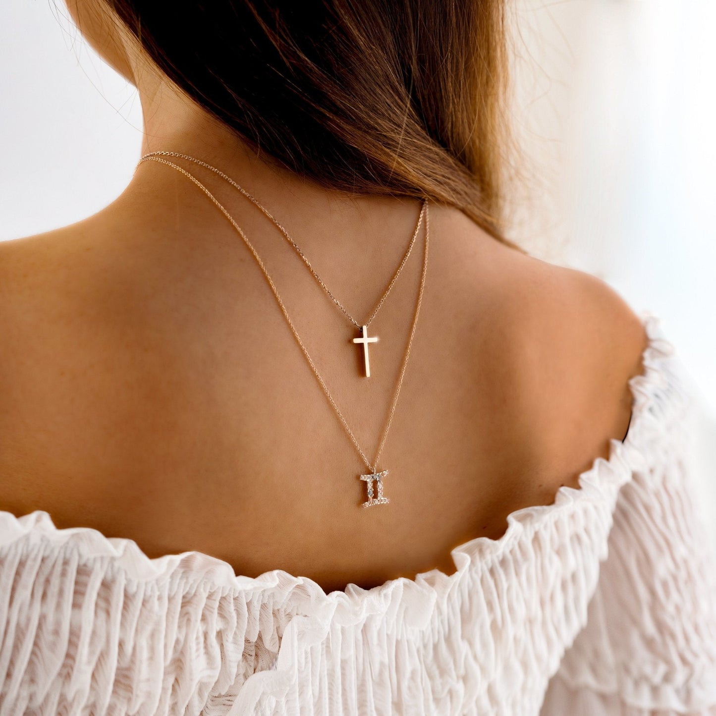 Frau mit goldener Kreuzkette und Zwillingsanhänger, eleganter Schmuck, weißes Kleid.