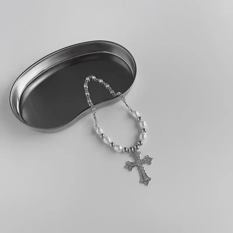 Silberne Kreuzkette mit Perlen auf Metalltablett, religiöser Schmuck, minimalistisch.