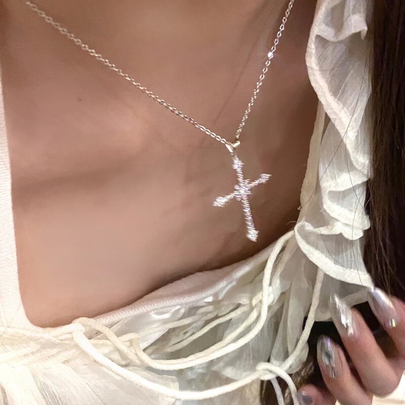 Silberne Kreuzkette mit Strasssteinen, getragen auf weißer Rüschenbluse, eleganter Schmuck.