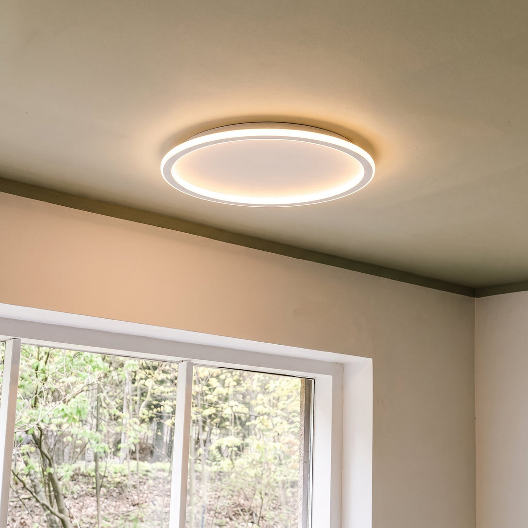 Rund loftslampe over et vindue med udsigt til grønne træer, tændt med varmt lys. 8