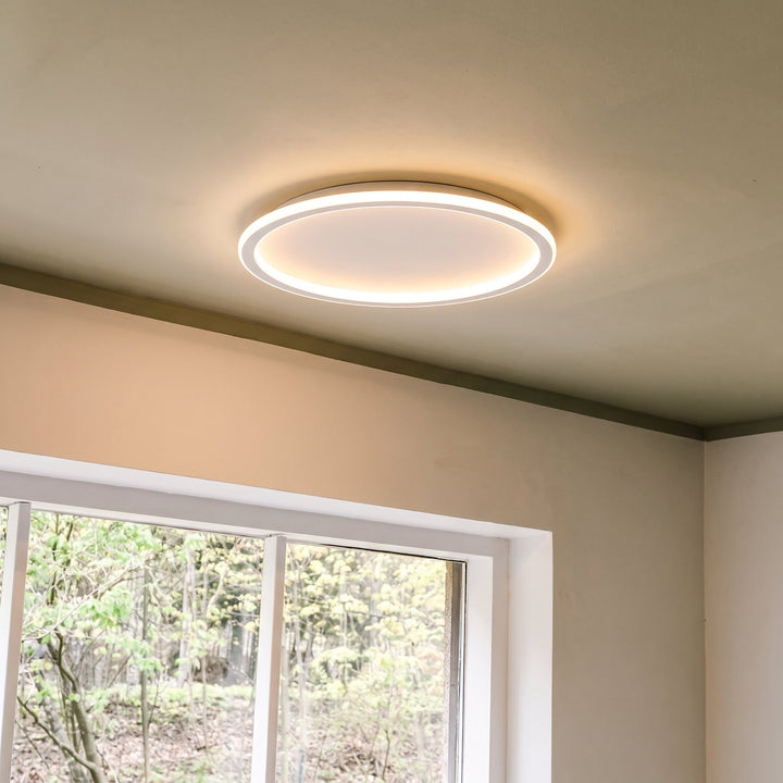 Rund loftslampe over et vindue med udsigt til grønne træer, tændt med varmt lys. 8