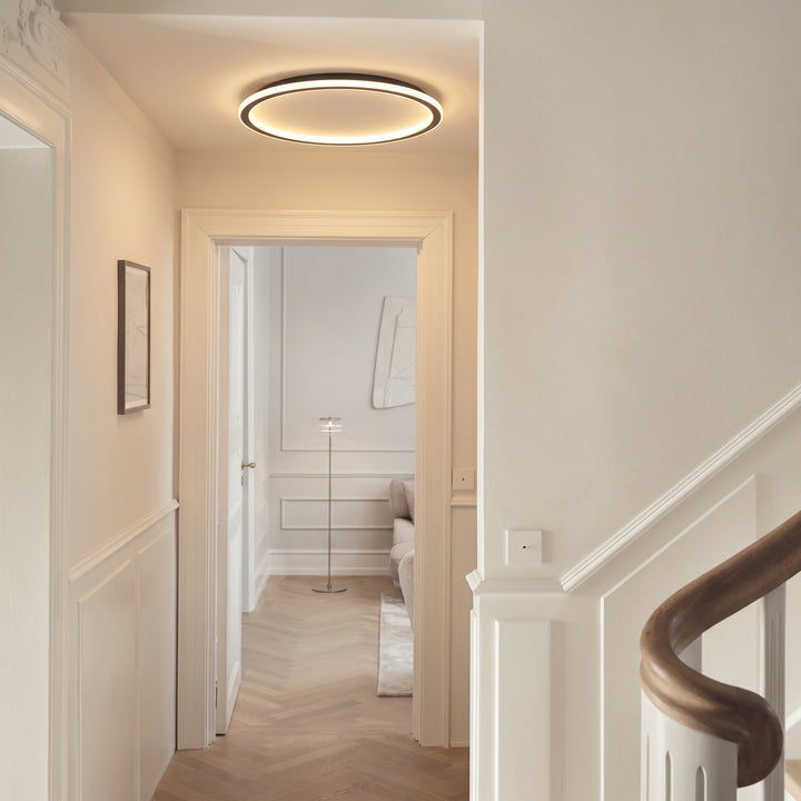 Tændt ringlampe i en lys gang med hvide lister, sildebensparket og en trappe med trærækværk. 5