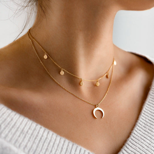 Frau trägt goldene Halskette mit Halbmond-Anhänger und kleinen runden Anhängern, eleganter Schmuck.