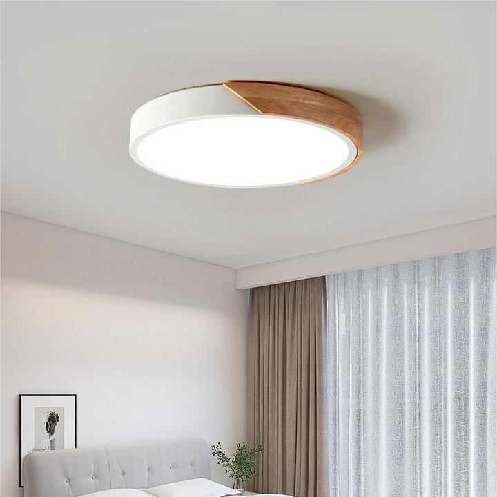 Hvid rund loftslampe med trædetalje i loftet over et soveværelse med gråt sengegavl og gardiner. 3