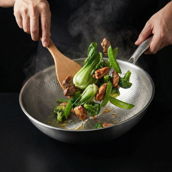 Hænder rører med en træspatel rundt i woken med kylling, pak choi, broccoli og sukkerærter under tilberedning. 7