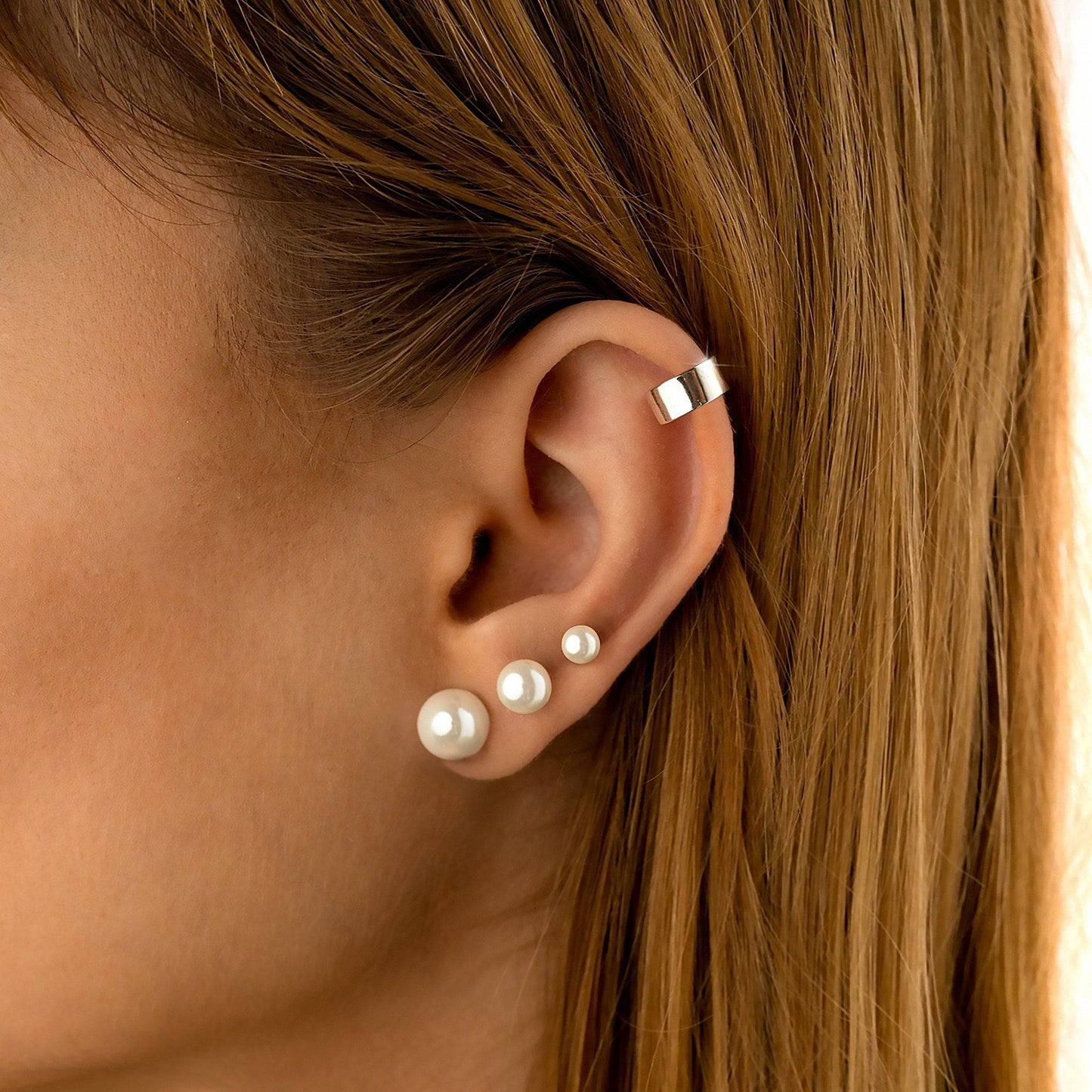Frau mit Perlenohrringen und silbernem Ohrclip, eleganter Schmuck, Nahaufnahme.