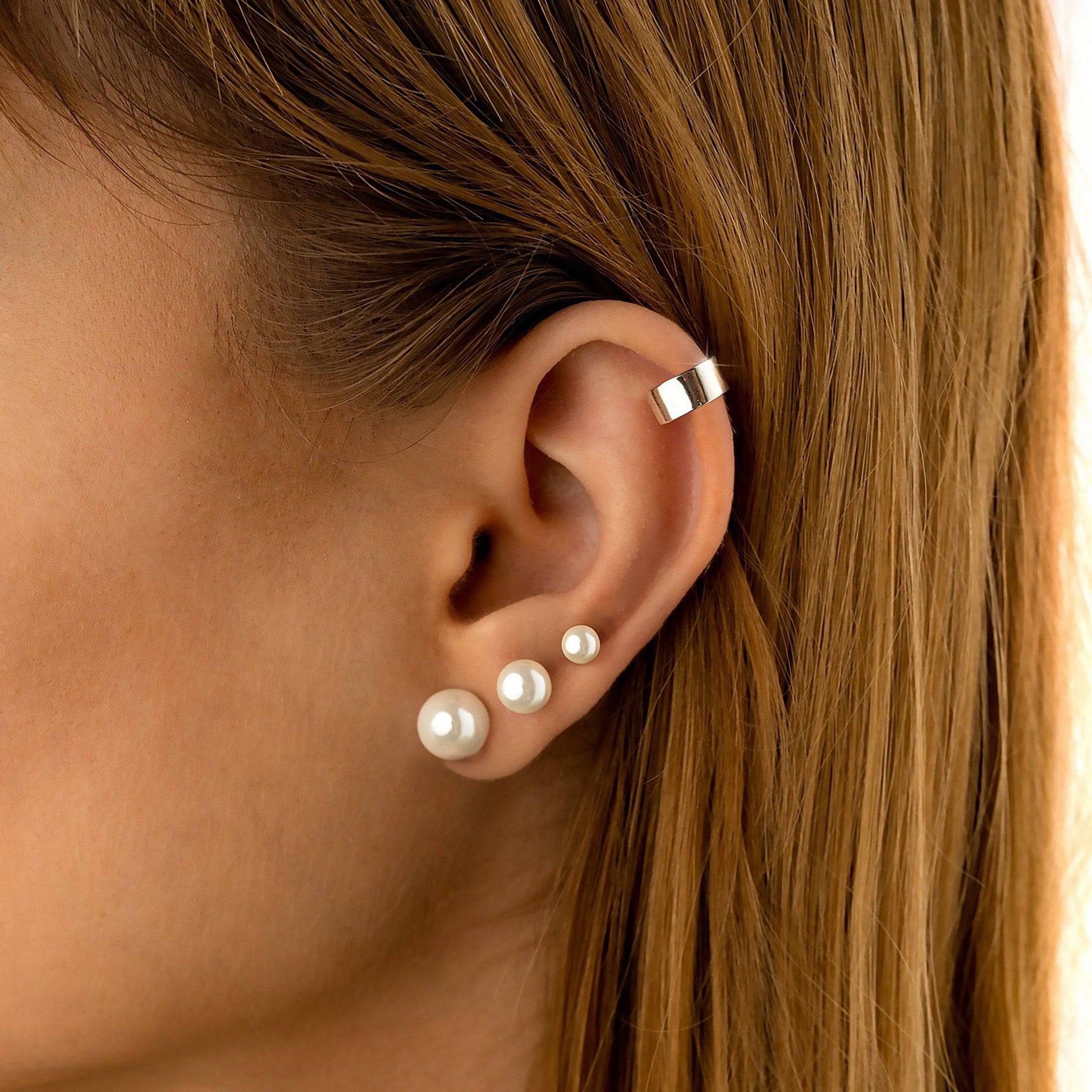 Frau mit Perlenohrringen und silbernem Ohrclip, eleganter Schmuck, Nahaufnahme.