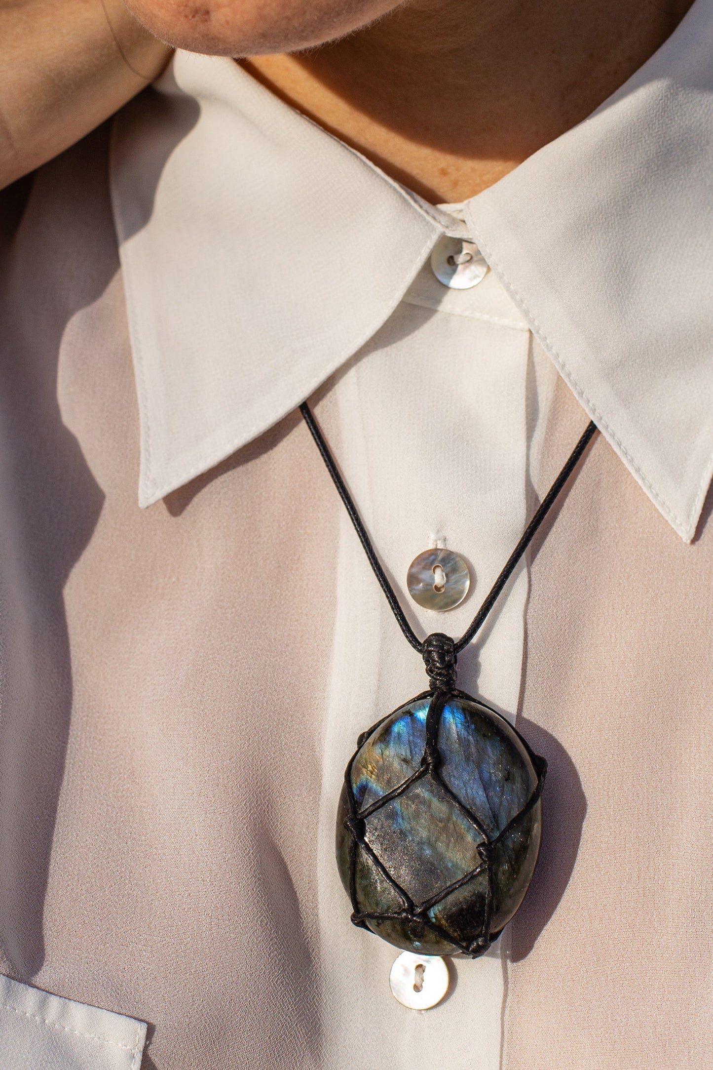 Labradorit-Anhänger an schwarzem Lederband, getragen auf weißer Bluse, Schmuck, Edelstein, Mode.